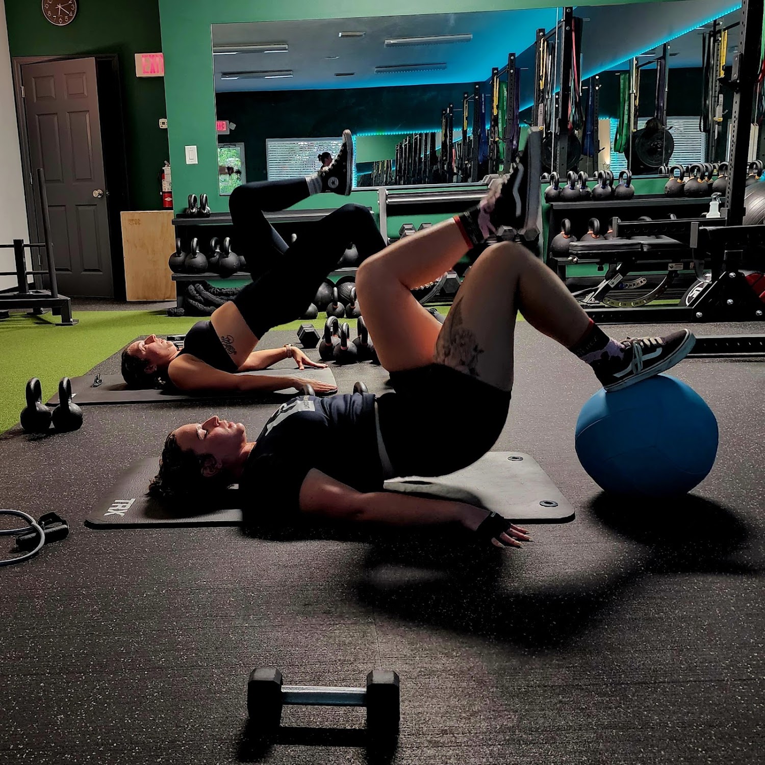 Members working through core exercises on mats inside Hour of Power Fitness, with kettlebell racks and mirrors along the far wall